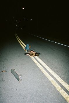 a person laying on the ground next to a skateboard in the middle of the road