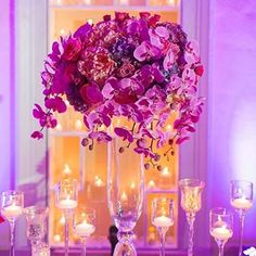 a tall vase filled with purple flowers on top of a table next to wine glasses and candles