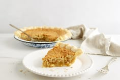 a piece of pie sitting on top of a white plate next to a fork and bowl