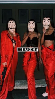 three women wearing red pants and masks with faces painted on them, standing in front of a garage door