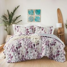 a bed with purple flowers on it in a room next to a wooden table and lamp