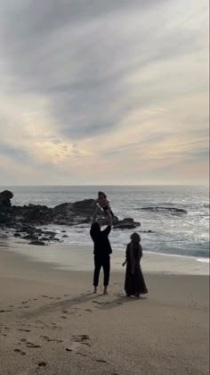 two people standing on the beach with a baby in their arms