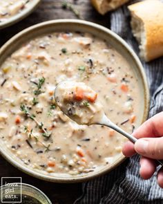 a hand holding a ladle full of creamy chicken and wild rice soup with bread in the background