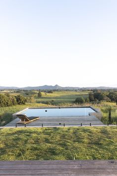 a wooden bench sitting on top of a lush green field next to a swimming pool