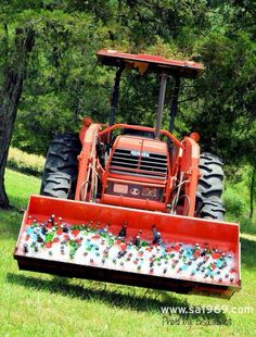 an orange tractor is parked in the grass next to some trees and flowers on it's front end