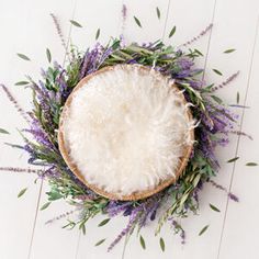 a basket filled with lots of purple flowers on top of a white wooden floor next to a plant