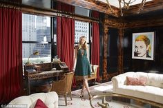 a woman standing in a living room next to a window with red drapes on it