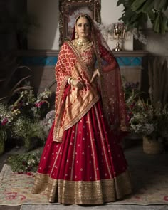 a woman in a red and gold bridal gown standing by a window with her hands on her hips