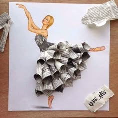 a woman in a dress made out of newspaper rolls on top of a wooden table