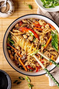 a bowl filled with noodles and vegetables on top of a wooden table next to chopsticks