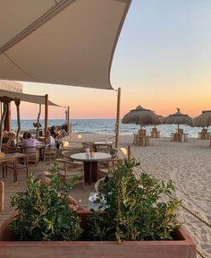 an outdoor dining area with tables and umbrellas on the beach near the ocean at sunset