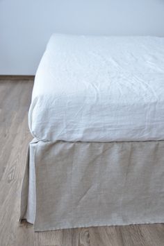 a bed with white linen on it and wood flooring in front of the headboard