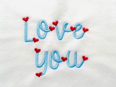 i love you written in blue and red thread on a white towel with hearts around it