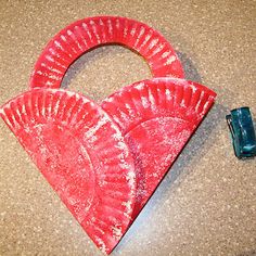 a red paper plate shaped like a heart next to a blue plastic toothbrush holder