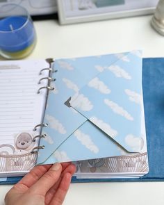 a person holding an open notebook with a paper airplane on it and a candle in the background