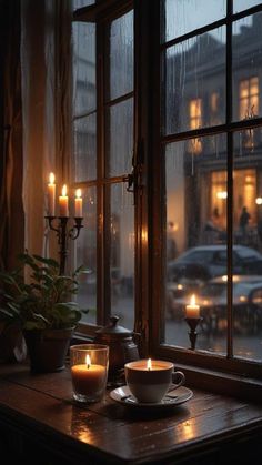 two teacups on a table in front of a window with candles lit up