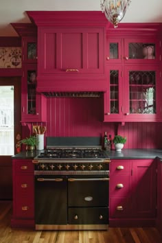 a kitchen with red cabinets and an oven in the center is painted bright pink, while a chandelier hangs from the ceiling