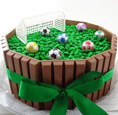 a cake decorated with soccer balls and green grass in a basket on top of a doily