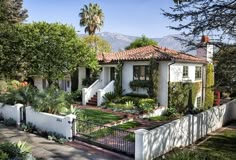 a white house surrounded by trees and greenery on a sunny day with mountains in the background