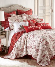 a bed with red and white comforters in a room next to a lamp on a table