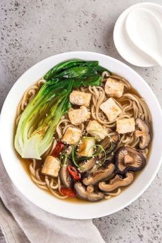 a white bowl filled with noodles, tofu and broccoli on top of a table