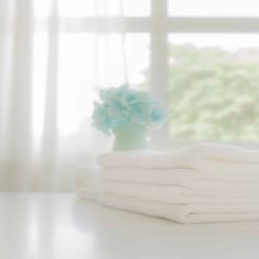 stack of folded white towels sitting on top of a table next to a vase with flowers