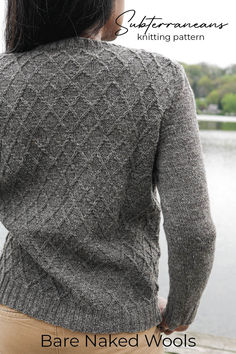 the back of a woman's sweater that has been knitted with yarn and is next to a body of water