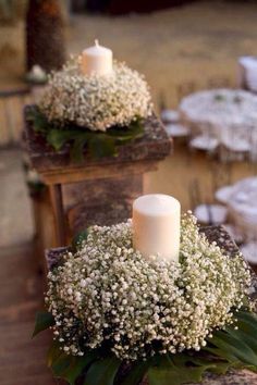 two white candles sitting on top of a wooden box filled with baby's breath