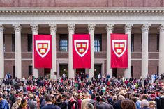 a large group of people standing in front of a building with two red flags hanging from it's sides