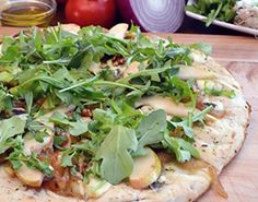 an uncooked pizza sitting on top of a wooden cutting board next to vegetables