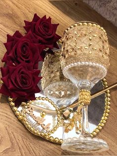 two wine goblets on a table with red roses in the background and gold accents