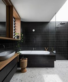 a bathroom with black tiled walls and flooring next to a bathtub in the corner