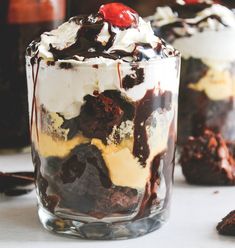 two desserts with chocolate, cream and cherries in them on a white table