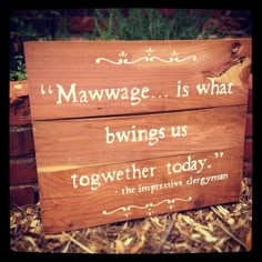 a wooden sign sitting in the grass next to a brick wall with words written on it