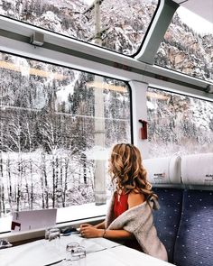 a woman sitting at a table on a train looking out the window with snow covered mountains in the background