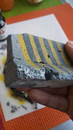 a hand holding a piece of cement with yellow stripes