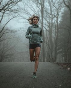 a woman running down a road in the woods on a foggy day with trees behind her