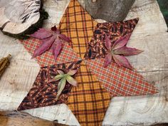 a patchwork star is sitting on top of a piece of wood with autumn leaves