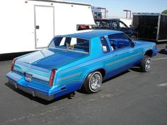 a blue car parked in a parking lot next to other cars and trailer behind it