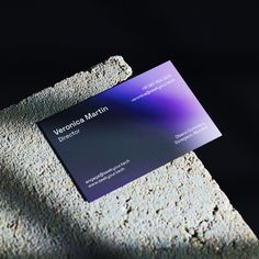 a purple business card sitting on top of a stone wall next to a black background