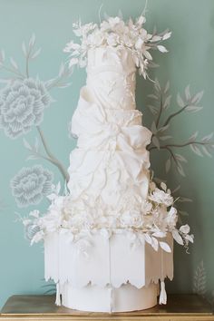 a white wedding cake on top of a wooden table next to a wall with flowers