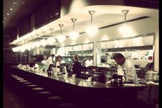 a group of people standing at a counter in a restaurant with lights on the ceiling