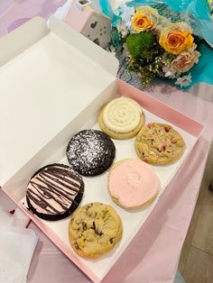 a box filled with assorted cookies and pastries on top of a pink table cloth