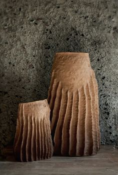 two brown vases sitting next to each other on a wooden floor in front of a stone wall