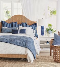 a bed with blue and white pillows in a bedroom next to a chair, table and window