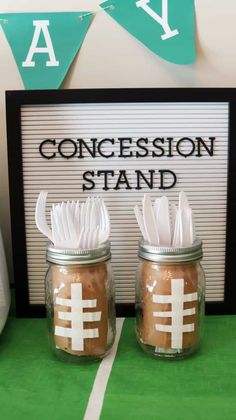 two mason jars with tissue paper in them are sitting on a green tablecloth and there is a sign that says, concession stand