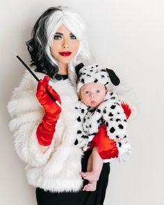 a woman holding a baby dressed in dalmatian clothing and wearing red gloves with her hand on top of her head