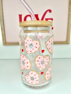 a glass jar filled with pink and white heart shaped donuts next to a straw