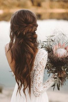 a woman with long hair holding a bouquet in front of her face and looking at the water