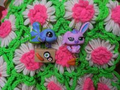 two little dolls are sitting on a crocheted blanket with pink and green flowers